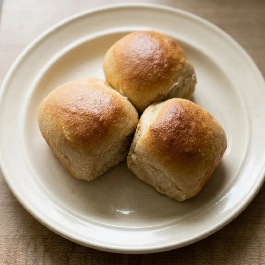 A plate of three milk kefir dinner rolls, their tops glistening with honey and sprinkled with sesame seeds.