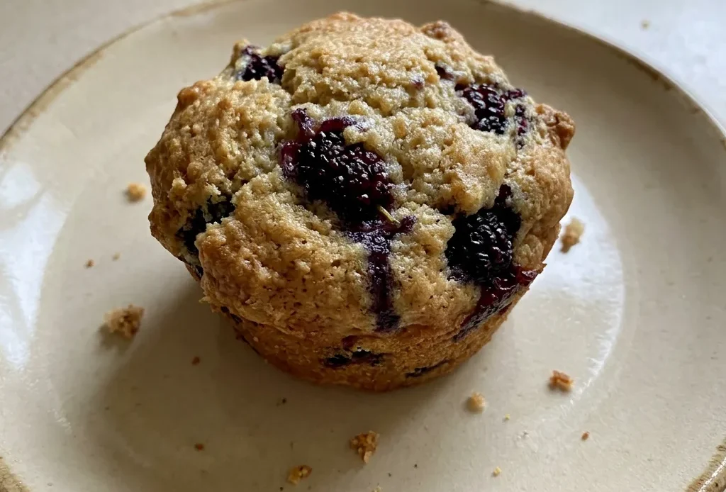 Bird's-eye view of three mulberry muffins with dark purple berries visible on top, one muffin cut in half showing purple berry swirls.