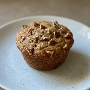 Looking down at a pecan pie muffin with a glossy brown top and pecan halves arranged in a circular pattern.