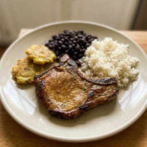 Looking down at three golden-brown pork chops arranged in a circle, each dusted with adobo seasoning and oregano, with garlic powder and olive oil glistening on the surface.