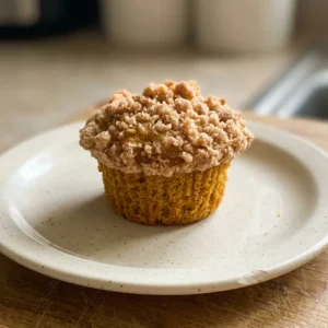 Looking down at two pumpkin muffins with crumb topping, one whole and one halved to show moist orange interior.