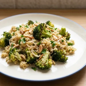 Top-down look at quinoa and broccoli salad with sliced almonds, parsley, and lemon wedges.