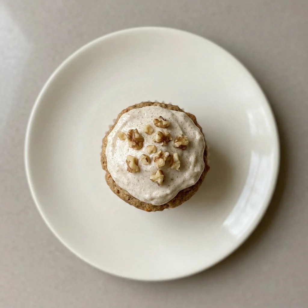 Ready to serve: a muffin crowned with cream cheese frosting, garnished with walnuts and carrot flecks.