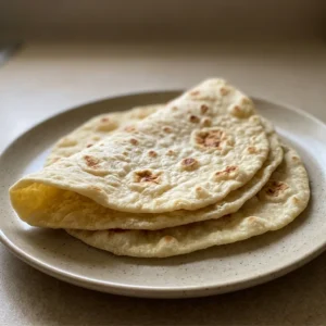 Overhead shot of two sourdough tortillas stacked, with visible char spots and a dusting of sea salt.