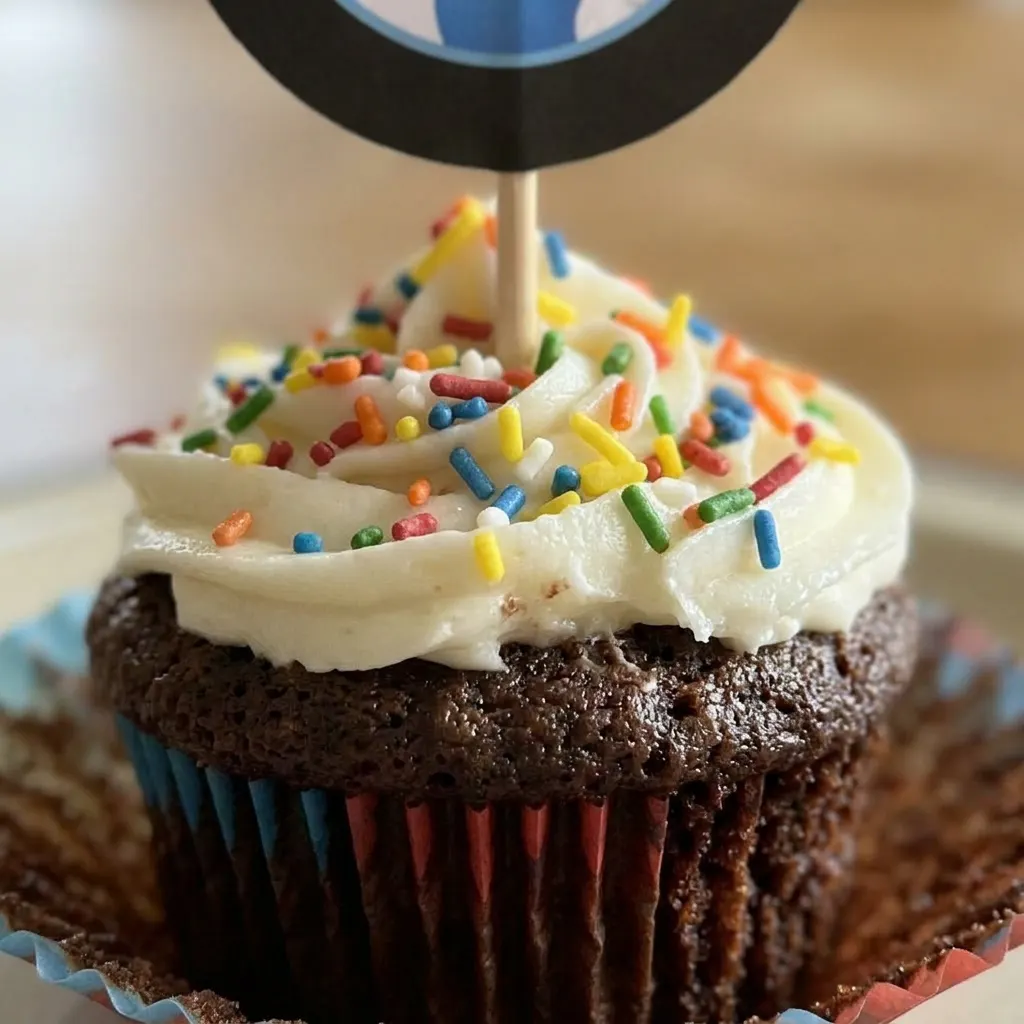 Zoomed in on a frosted chocolate cupcake with rainbow sprinkles, frosting swirl visible.