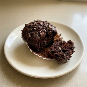 Bird's-eye view of a round brownie muffin with a cracked top, cocoa powder dusting, and visible chocolate chunks and chips.