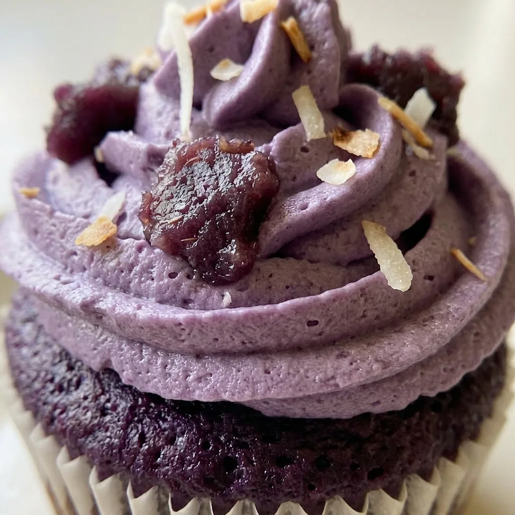 Zoomed in on a single ube cupcake with glossy purple frosting, a generous spoonful of ube jam, and a drizzle of heavy cream on top.