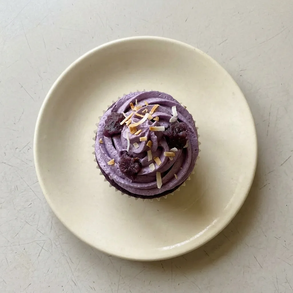 Ready to serve: two ube cupcakes on a white plate, their purple frosting topped with ube jam and a creamy swirl, with a side of extra jam.