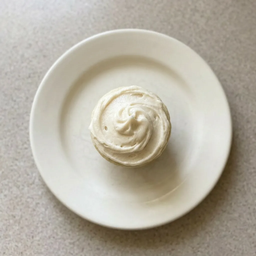 Plated single vanilla cupcake cake slice with thick vanilla buttercream topping.