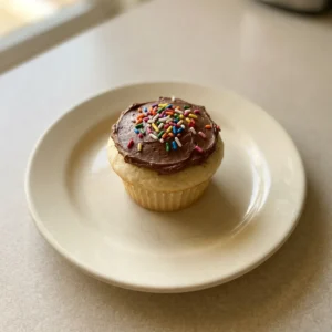 Bird's-eye view of three vanilla cupcakes with white frosting and rainbow sprinkles on a white plate.