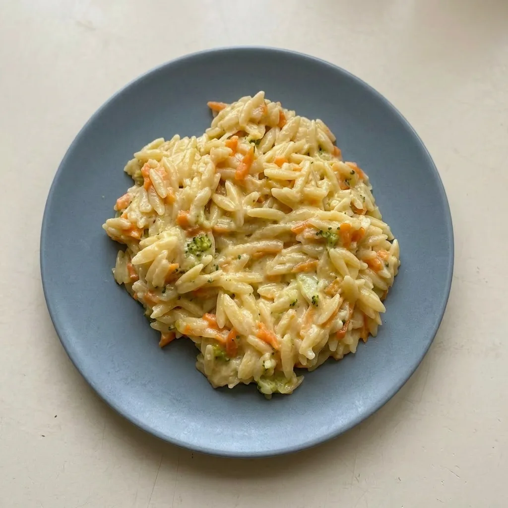 A plate of orzo with broccoli and carrots, garnished with cream cheese and parmesan.