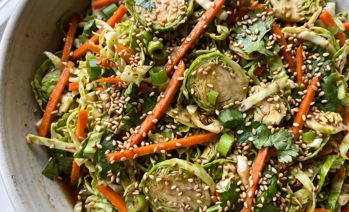 Asian shaved Brussels sprouts salad with shredded carrots, chopped cilantro, sliced green onions, and sesame seeds.