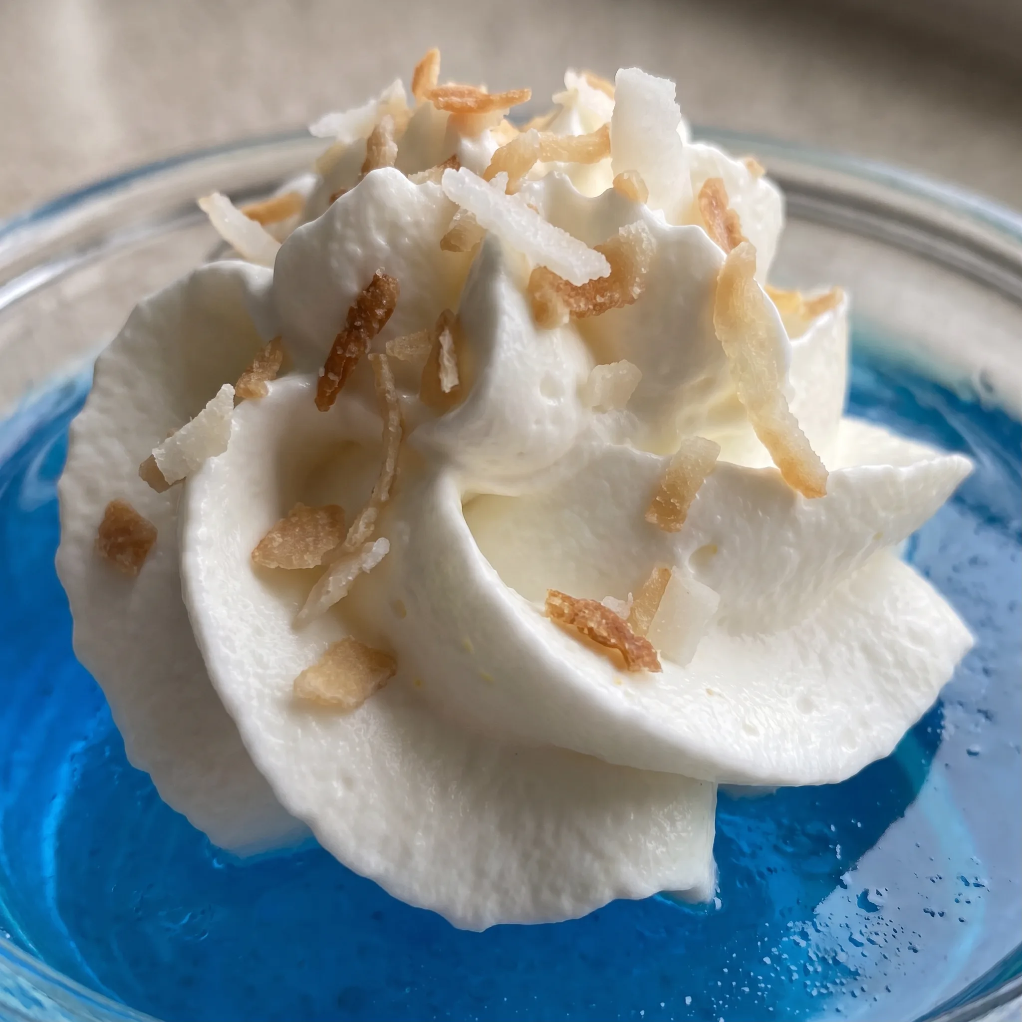 Creamy white swirl over blue gelatin, scattered with crisp toasted coconut shreds.