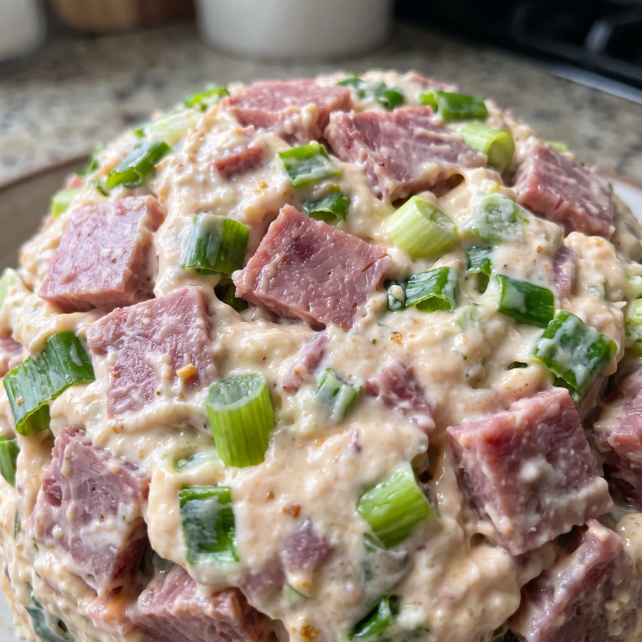 Creamy cheese ball surface dotted with green onion bits and shredded cheddar, wrapped in dried beef.