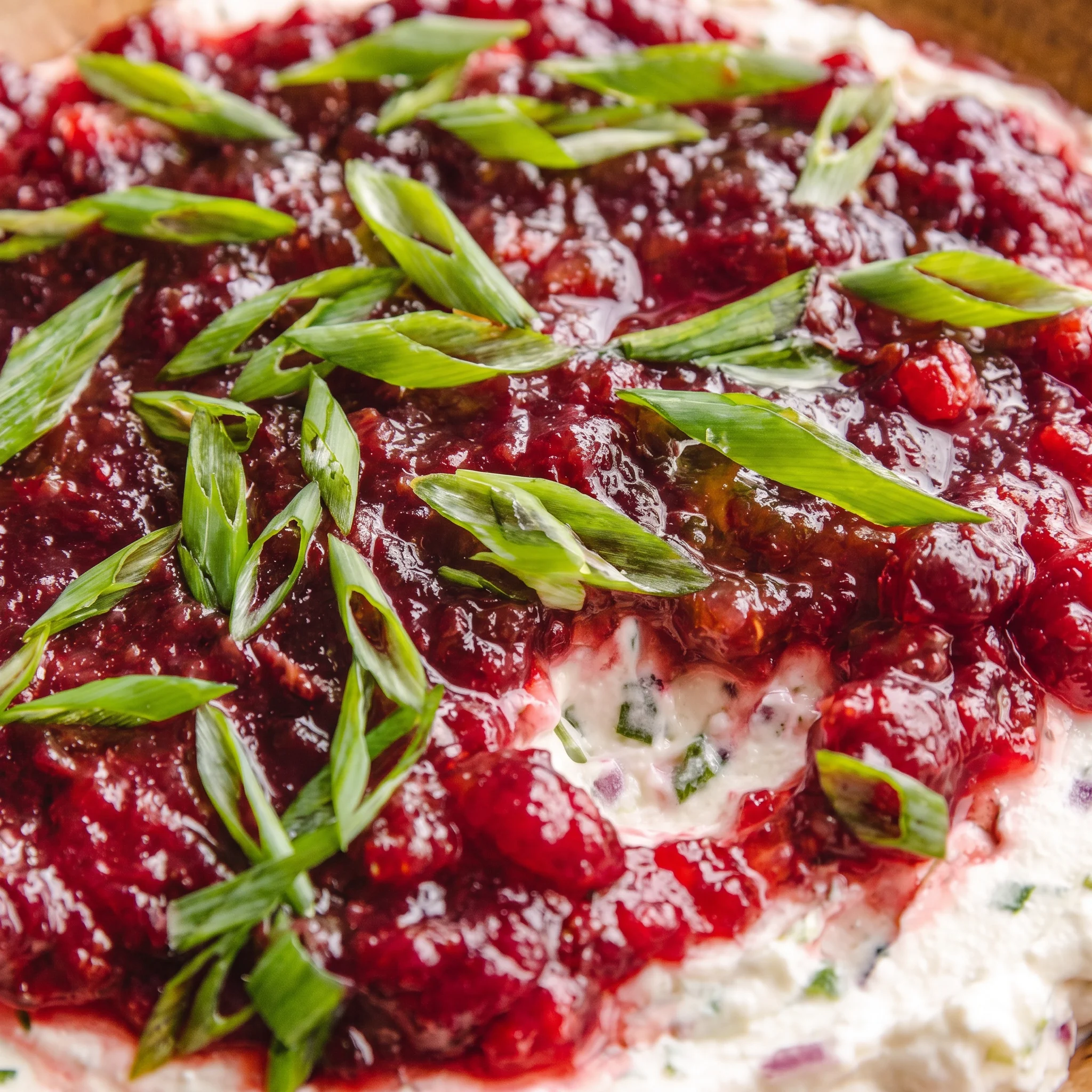 Smooth cream cheese dip marbled with chunky red cranberry sauce and scattered bits of green jalapeño, with a glossy sheen and visible cranberry seeds.