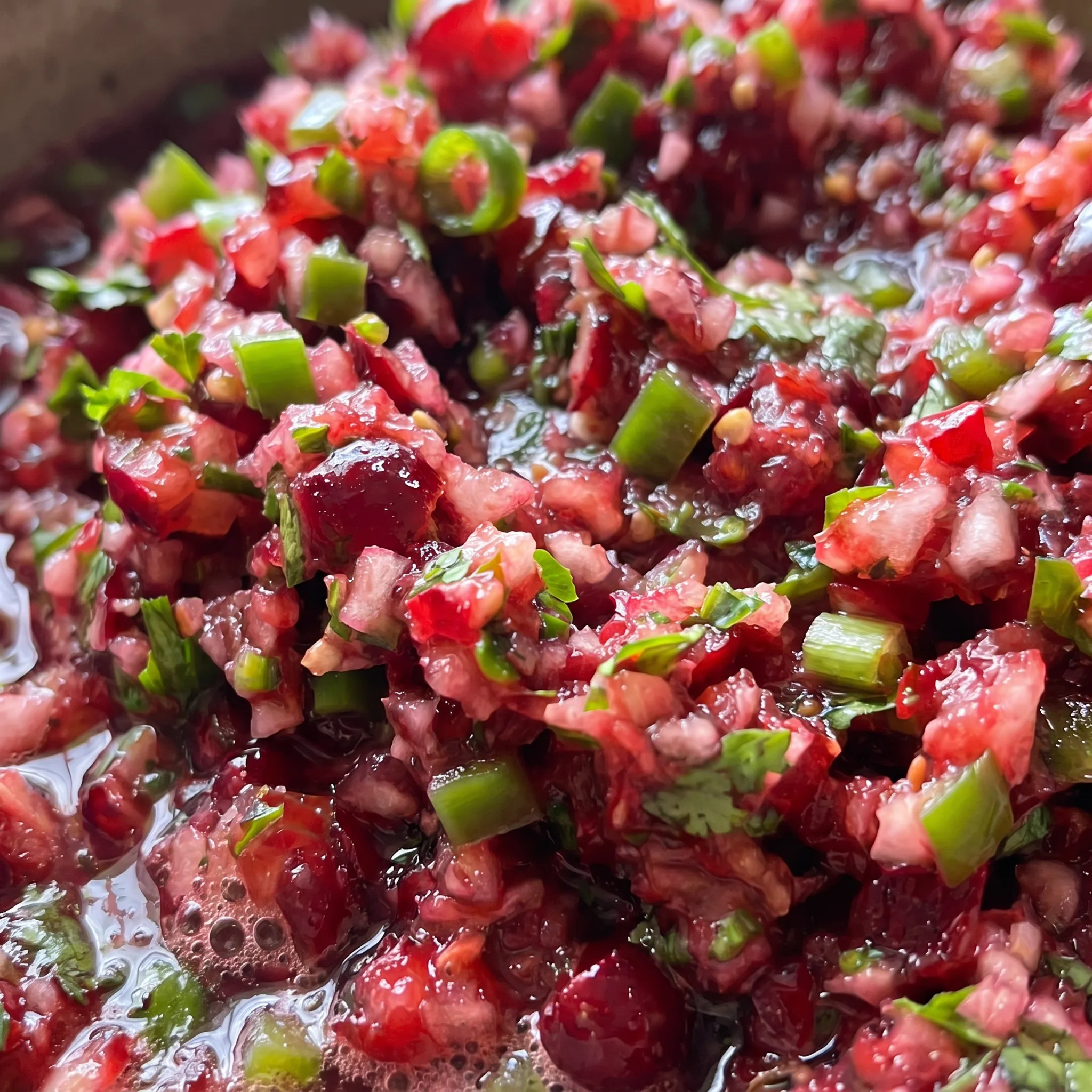 Chunky cranberry jalapeño salsa showing glossy cranberries and diced jalapeños with visible ginger bits.