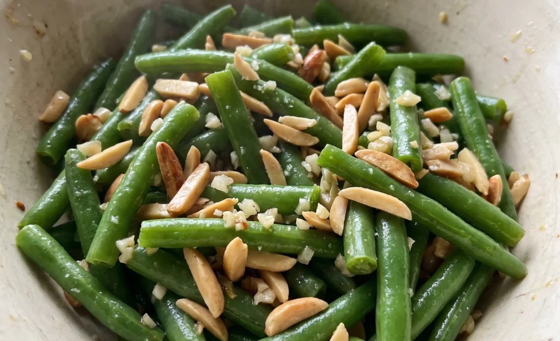 Green beans almondine with whole green beans, toasted almond slices, minced garlic, and butter sauce.