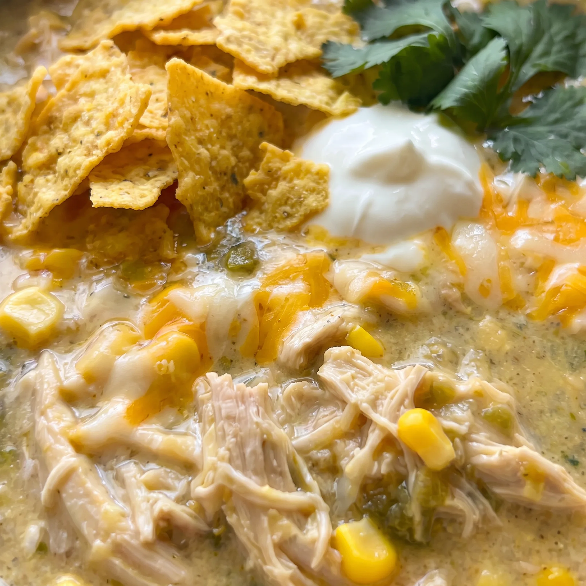 Creamy green soup with visible shreds of chicken, white beans, and corn kernels, topped with a swirl of cream cheese.