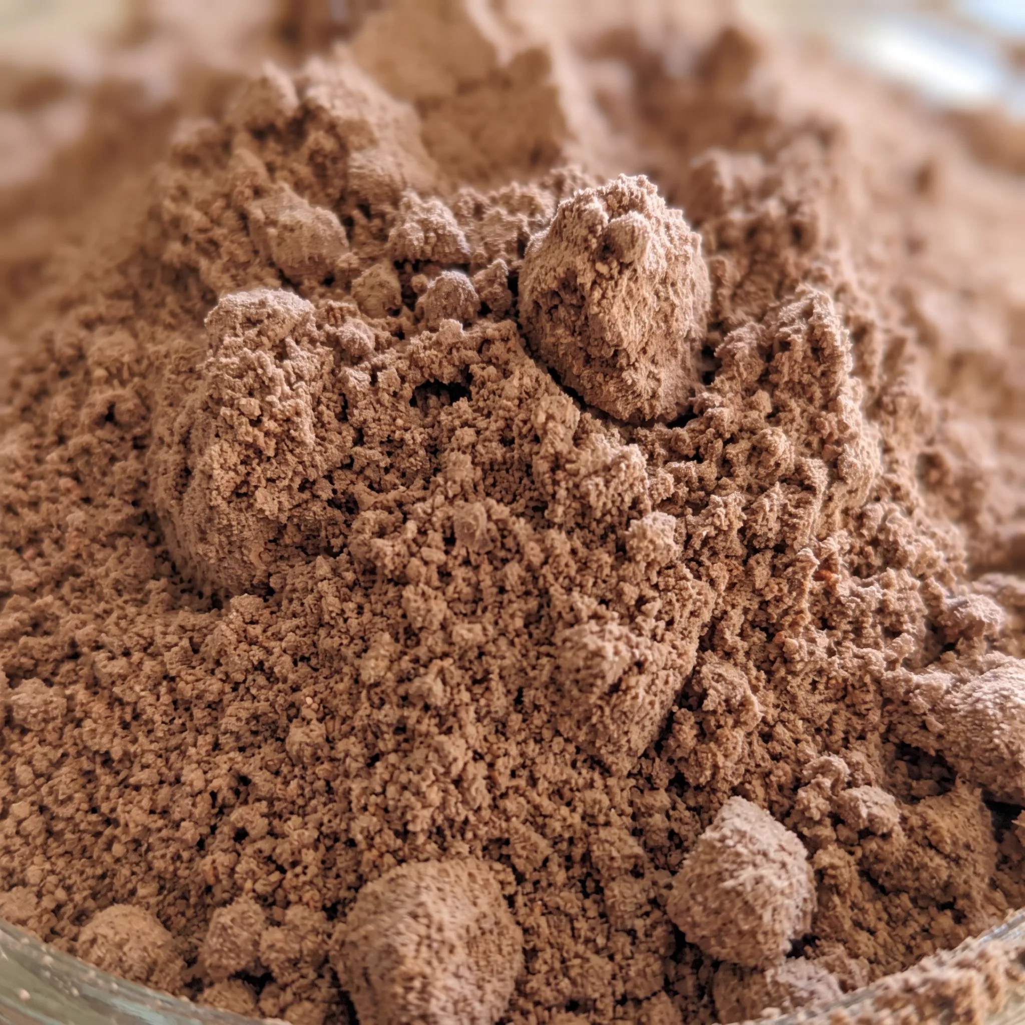 Cocoa powder and powdered milk form a grainy, speckled mixture with rich brown and creamy white patches.