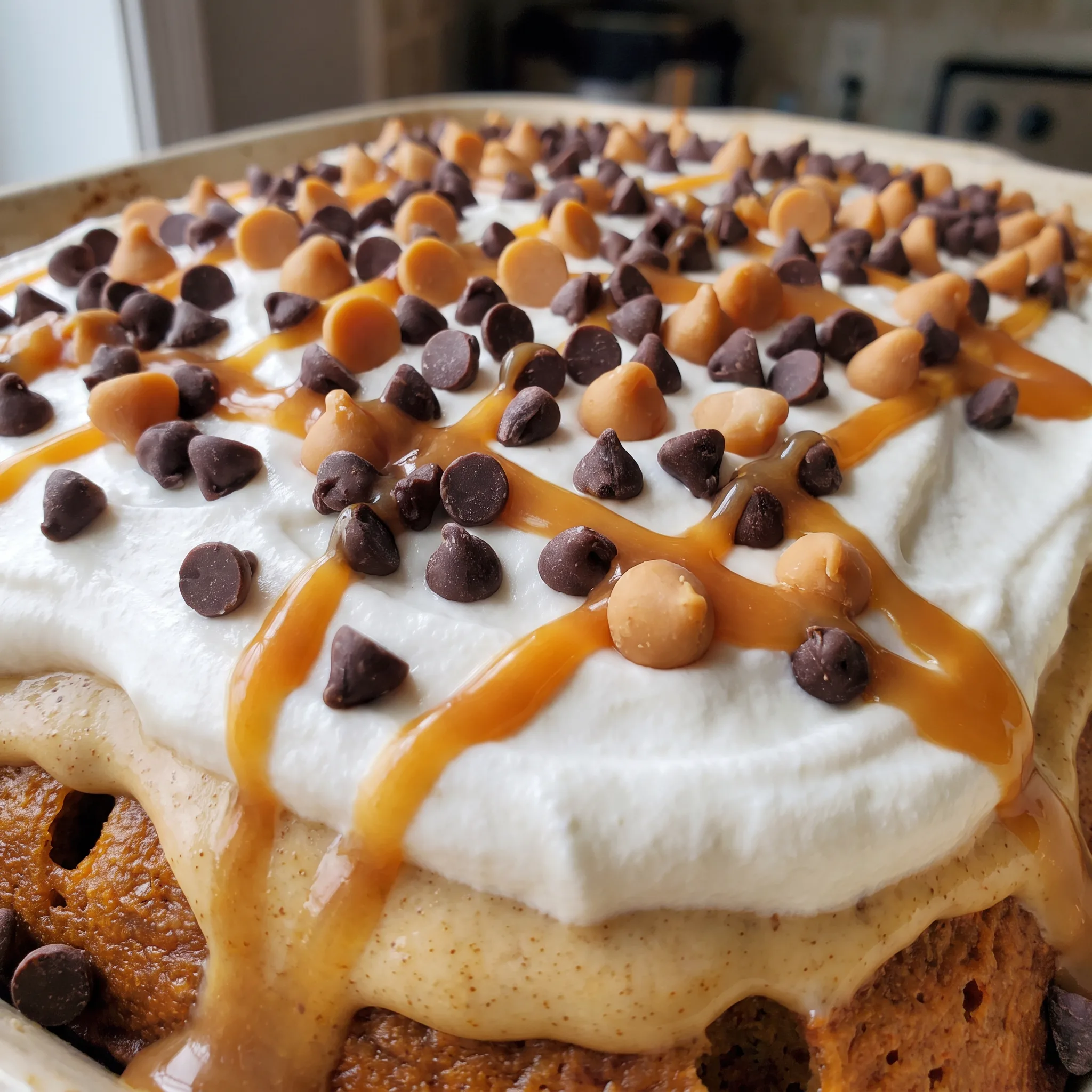 Moist pumpkin cake with creamy frosting, topped with whipped topping, chocolate and caramel chips, and a drizzle of caramel.