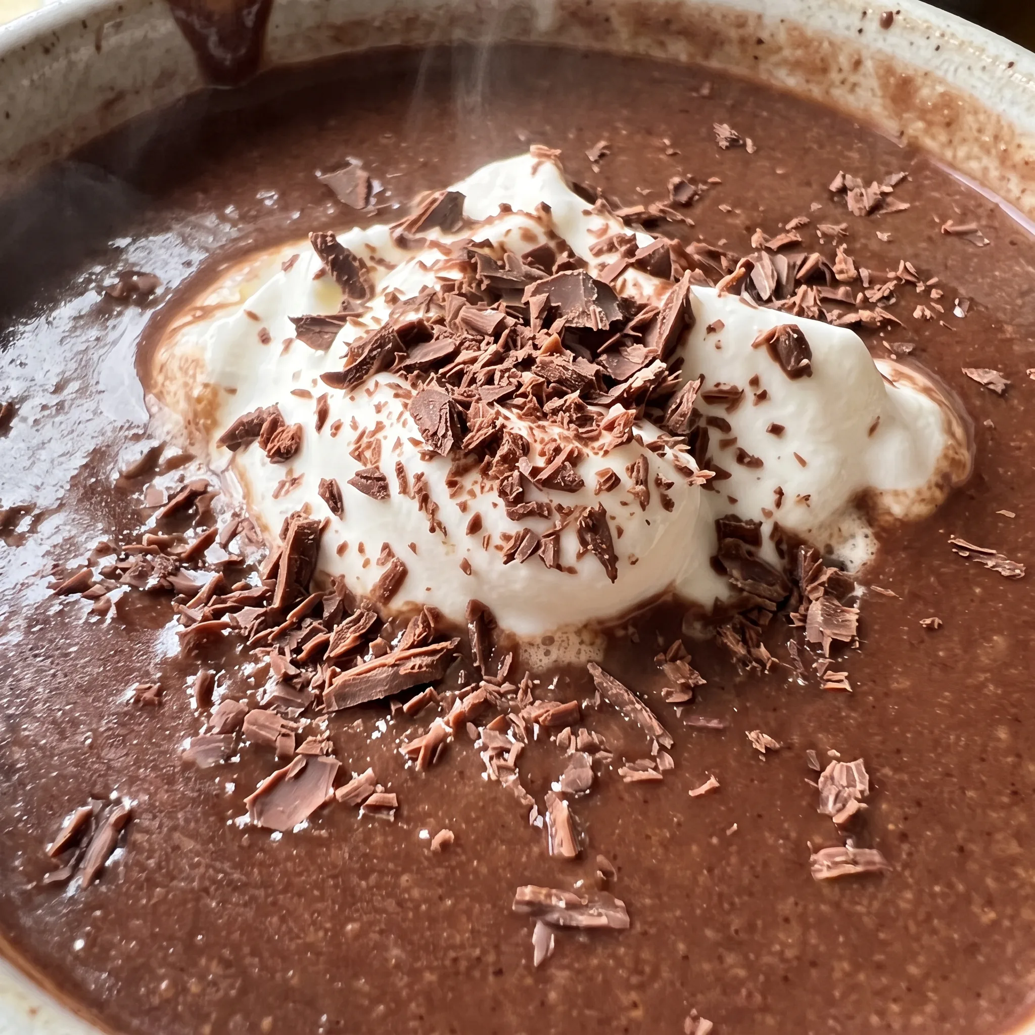 Silky hot chocolate with glossy surface, cocoa powder speckles, and melted chocolate chips swirling in smooth liquid.