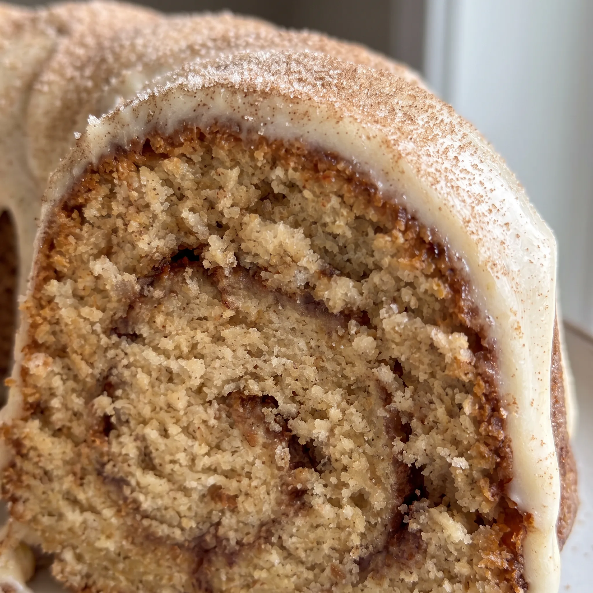 Cream cheese glaze drips down a cinnamon sugar crust over a cinnamon swirl Bundt cake.