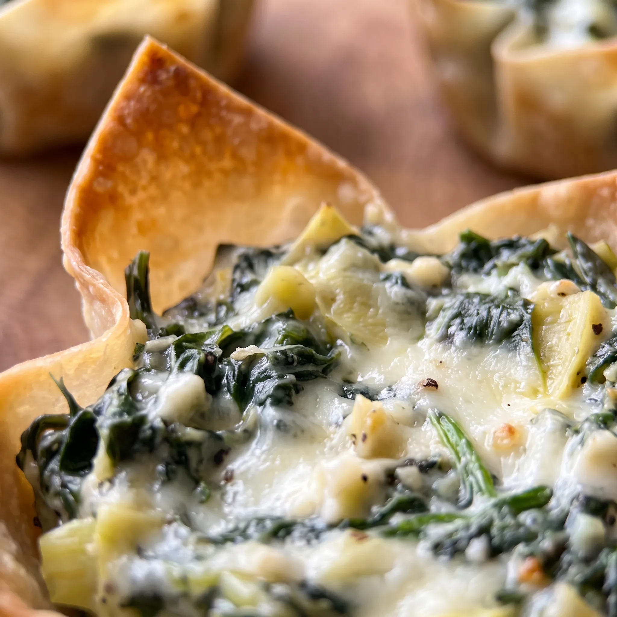 Golden baked wonton cups with soft cream cheese, chopped spinach, and artichoke hearts, sprinkled with Parmesan.