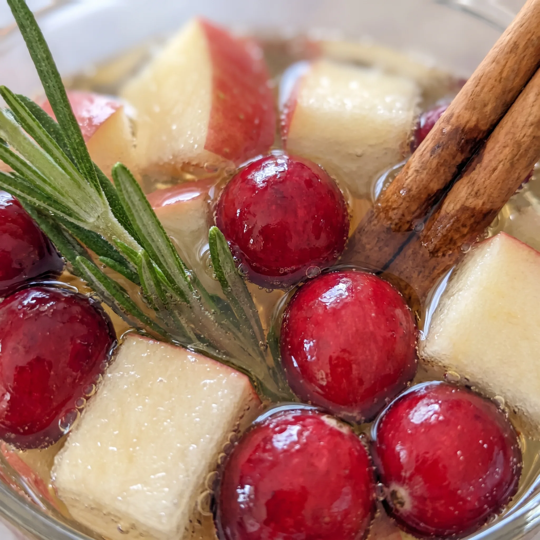 Clear white wine with floating cranberries, a translucent apple slice, and a cinnamon stick.