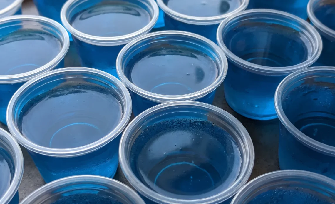 Berry blue Jell-O shots in small cups, bright blue gelatin with a smooth glossy surface and a hint of peach schnapps and rum.