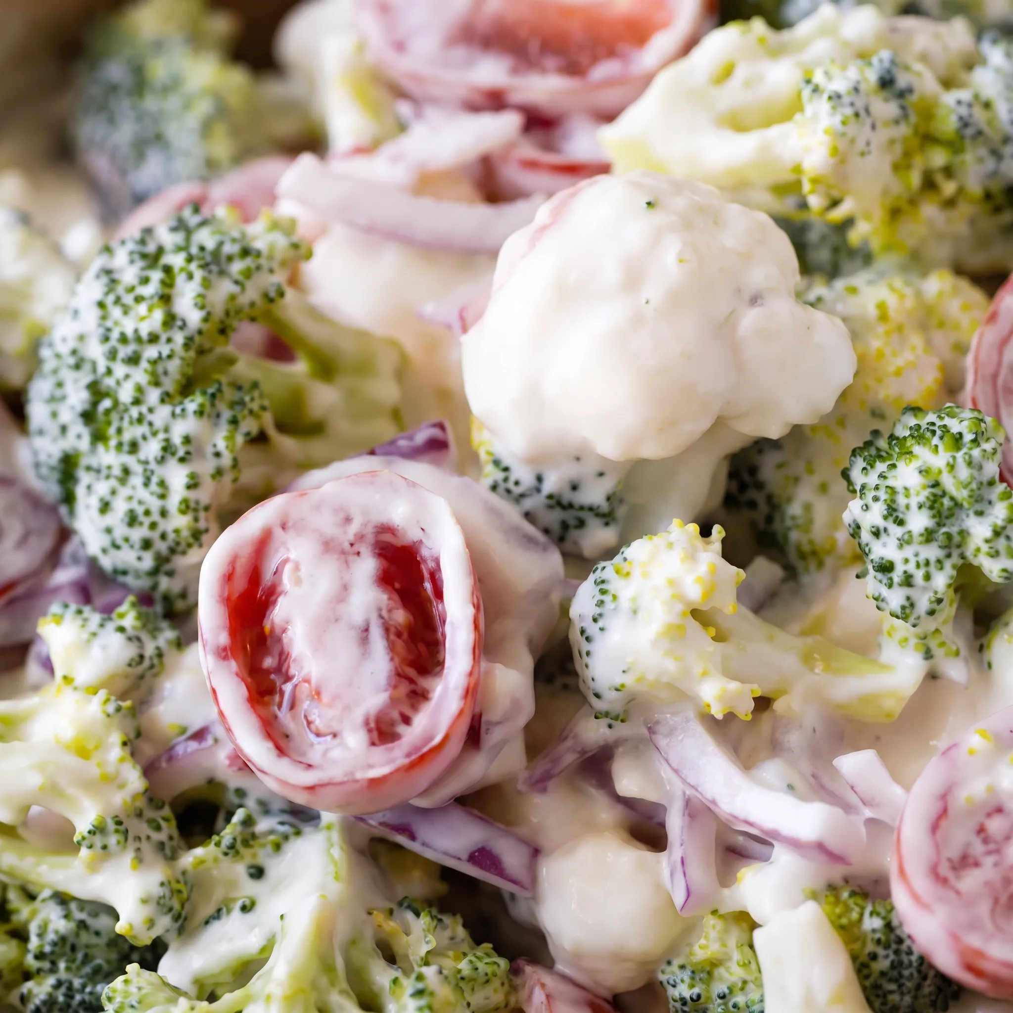 Creamy white dressing coating broccoli and cauliflower florets with halved cherry tomatoes and red onion.