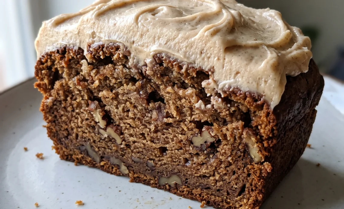 Sliced brown butter banana bread topped with cream cheese frosting and scattered pecan pieces.