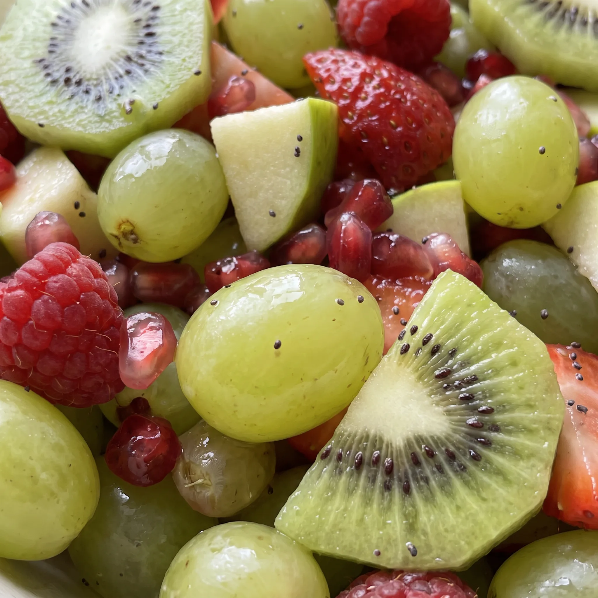 Glossy raspberries and strawberries with juicy pomegranate arils and green grapes, soft kiwi chunks, glistening fruit.