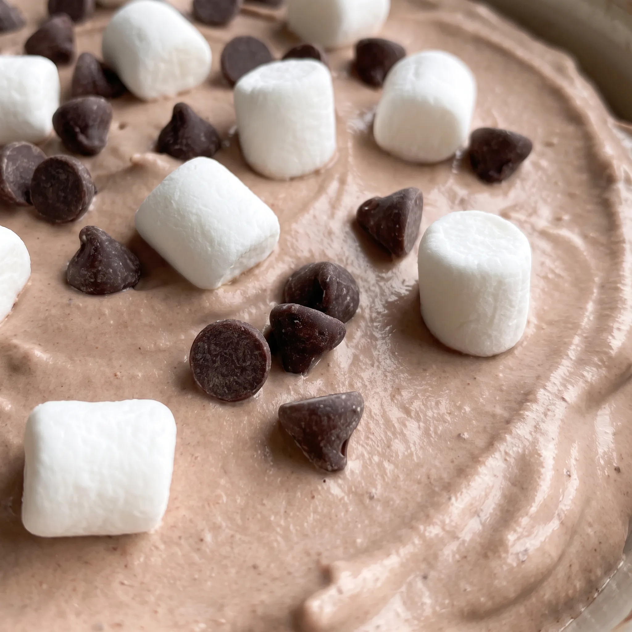 Swirls of fluffy brown dip with mini marshmallows and chocolate chips resting on the soft, airy surface.