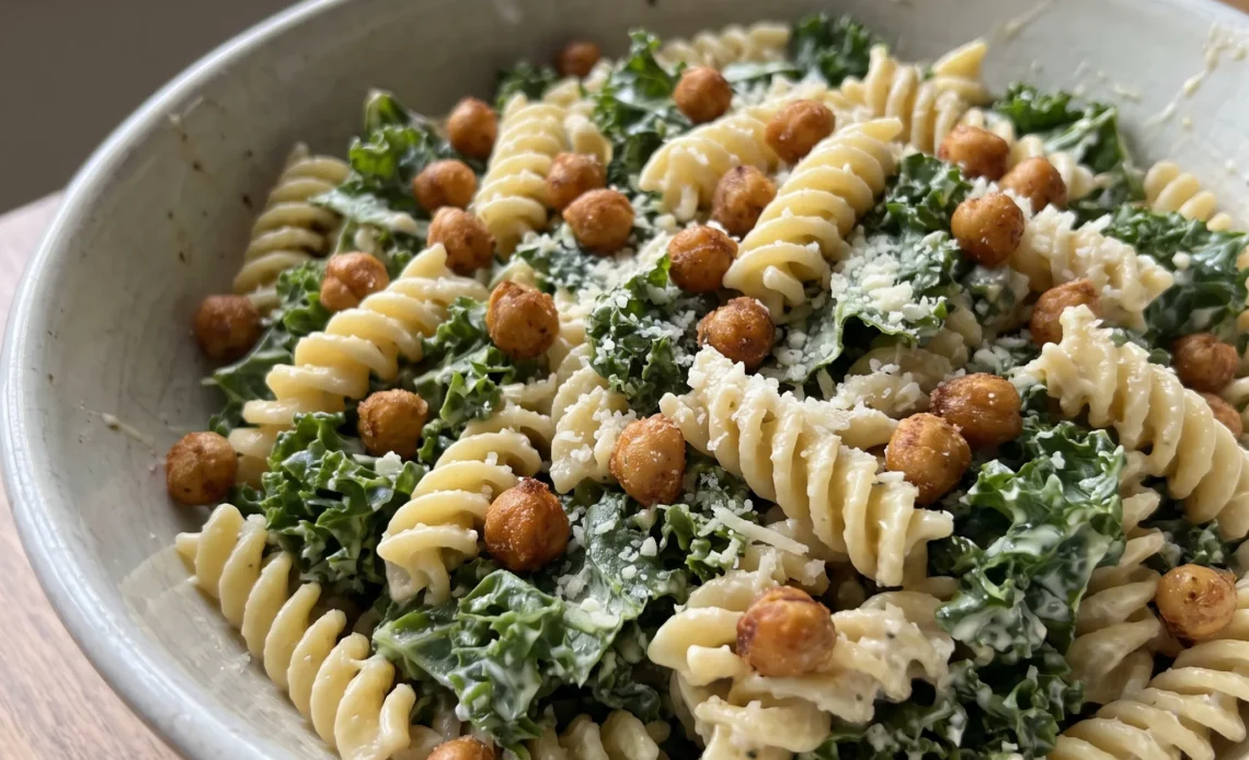 Kale caesar pasta salad with chickpeas, shredded Parmesan, and creamy Caesar dressing tossed together.