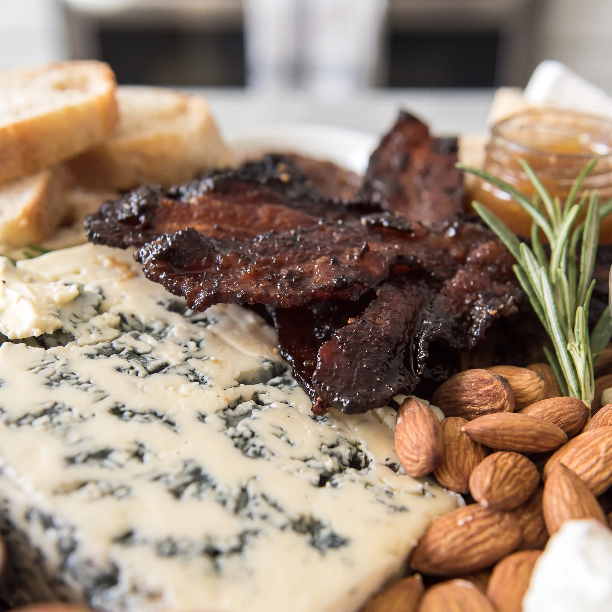 Glossy candied bacon strips with red sriracha glaze beside soft brie and crumbly blue cheese.