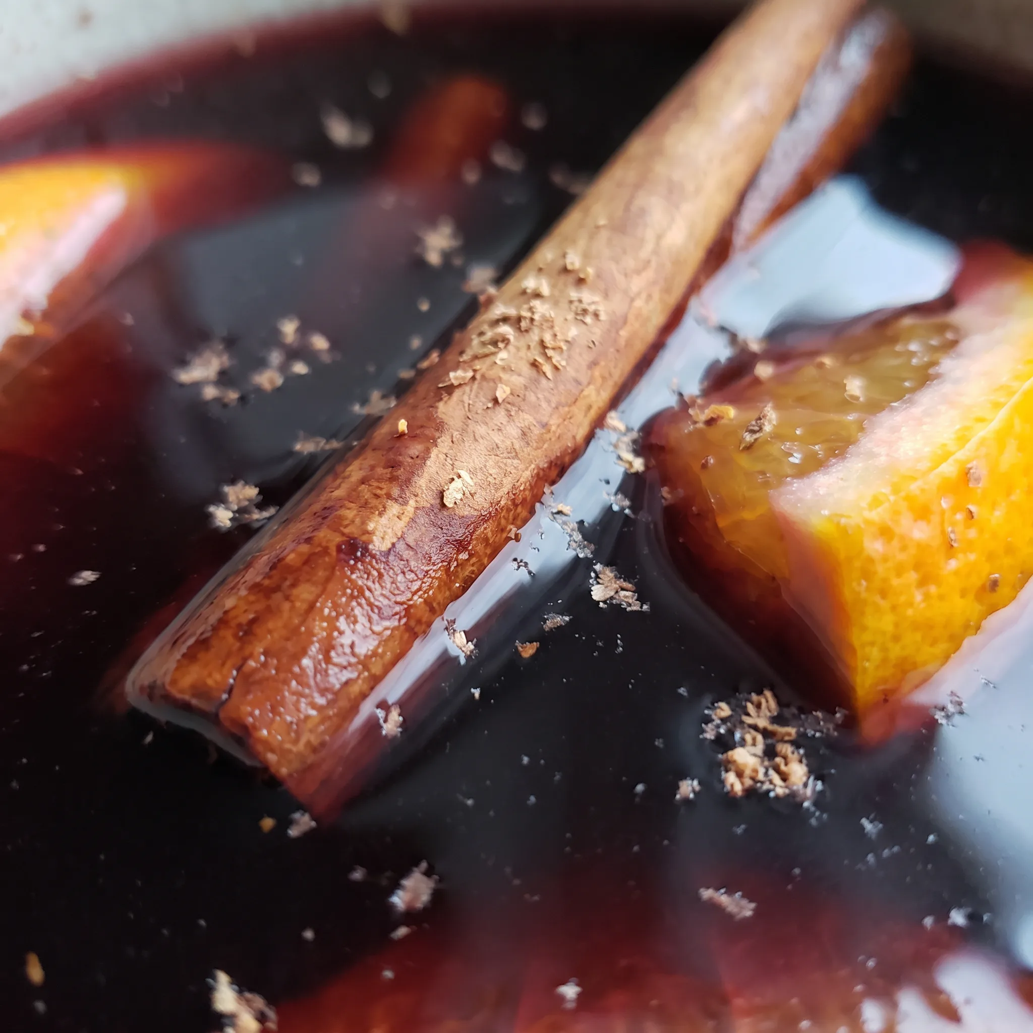 Glossy deep red mulled wine, translucent orange and grapefruit slices, a curled cinnamon stick resting at the edge.