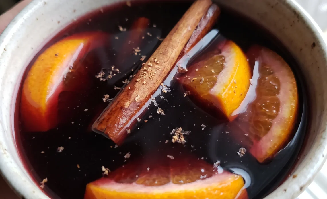 Mulled red wine with orange and grapefruit slices and a cinnamon stick, deep ruby liquid with citrus wheels floating on top.