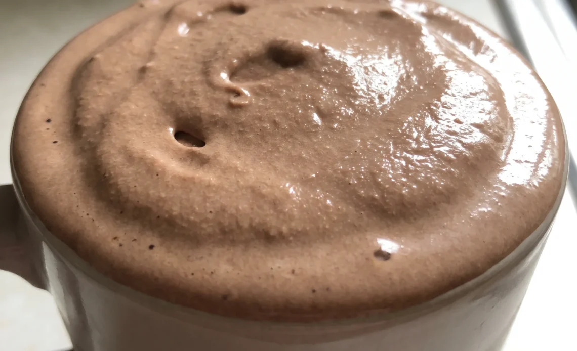 A chocolate frosty in a cup, thick and creamy, topped with a swirl of Cool Whip, pale white against the dark brown chocolate.