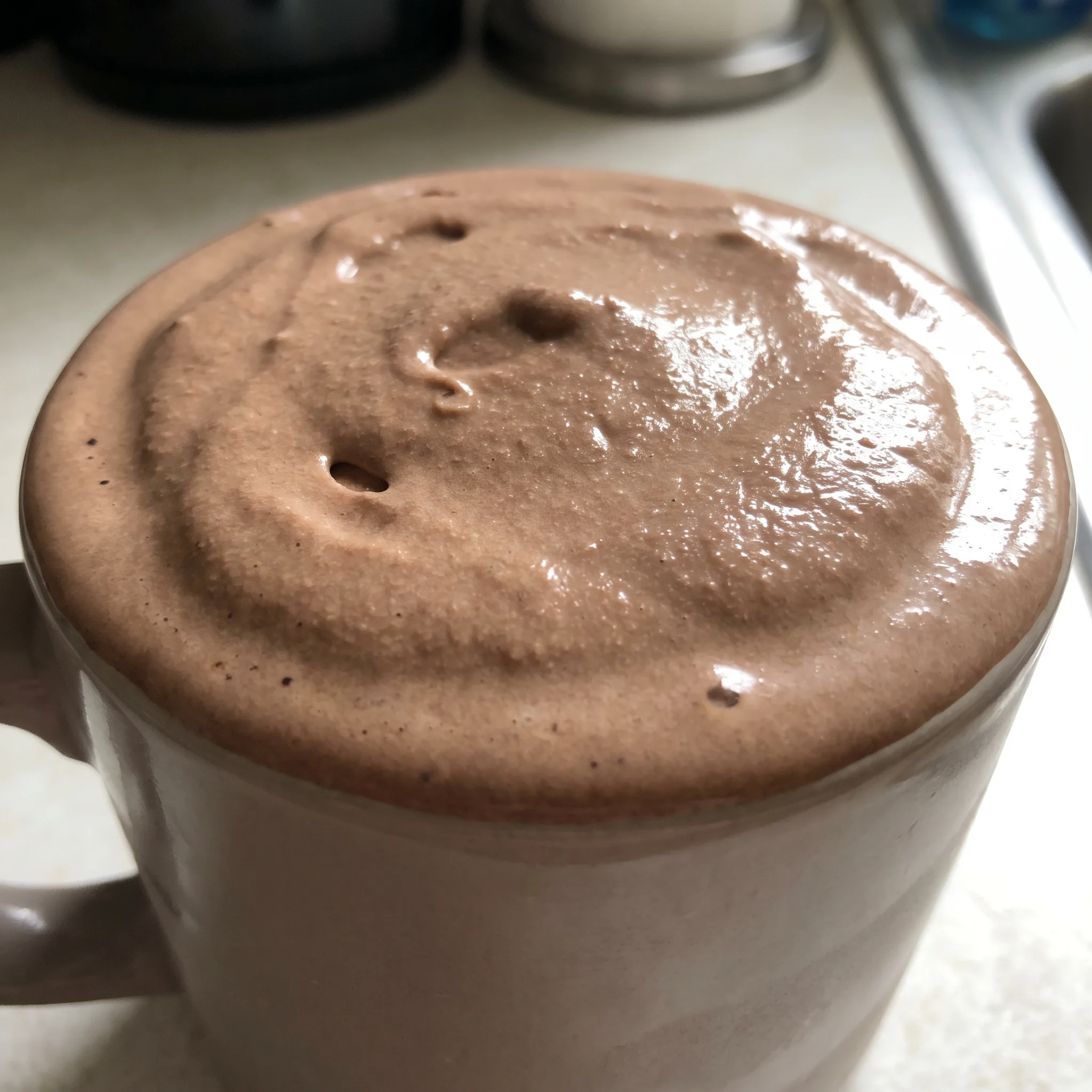 A chocolate frosty in a cup, thick and creamy, topped with a swirl of Cool Whip, pale white against the dark brown chocolate.