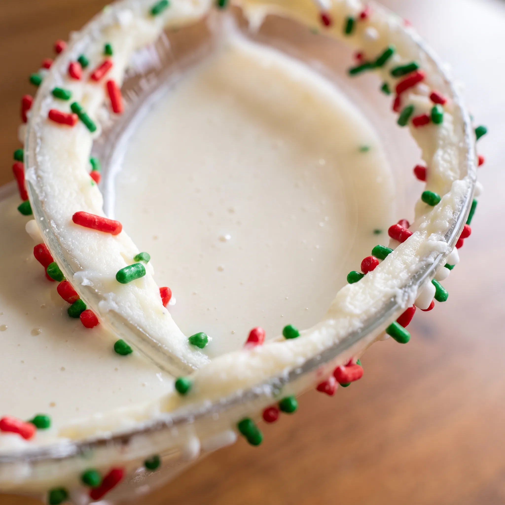 Creamy beige cocktail topped with white frosting and colorful sprinkles along the glass edge.