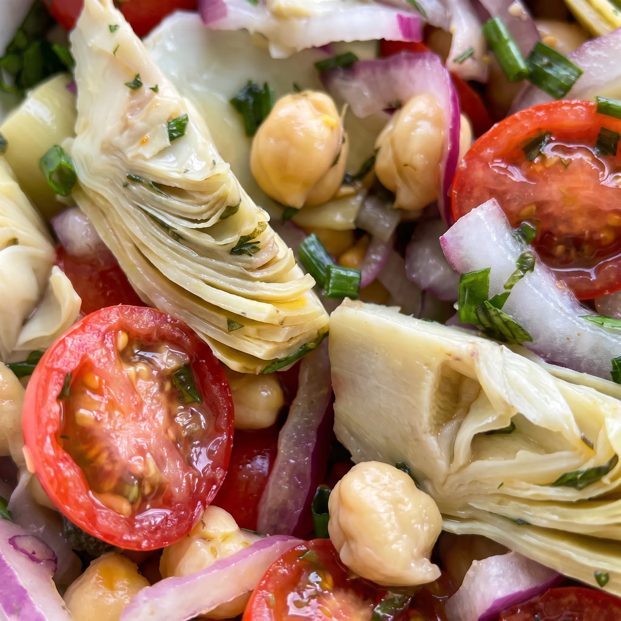 Glossy cherry tomatoes and chickpeas with tender artichoke pieces, crisp red onion, and green basil leaves.