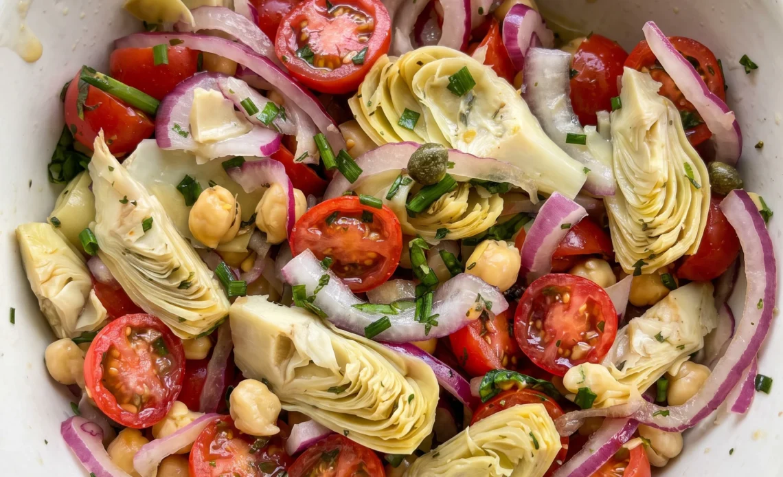 Tuscan chickpea artichoke tomato salad with cherry tomatoes, artichoke hearts, red onion, and basil.